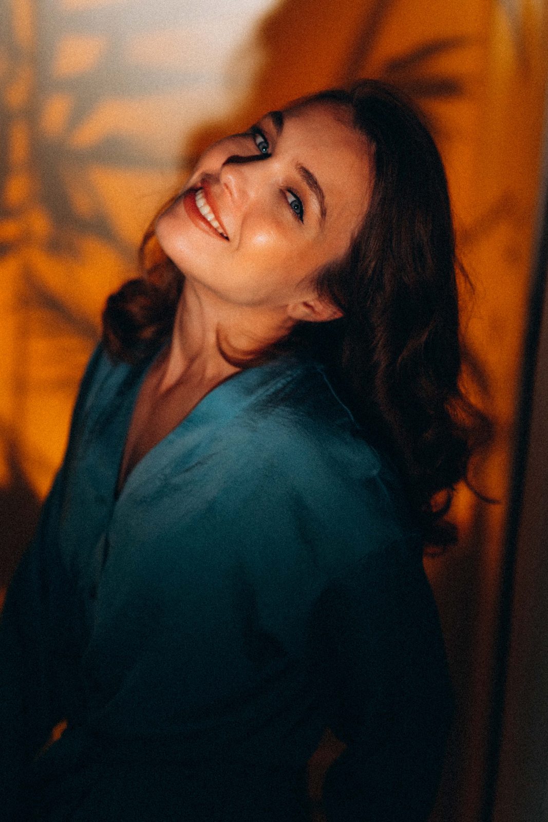 Smiling woman in a teal shirt against an amber wall with leaf shadows
