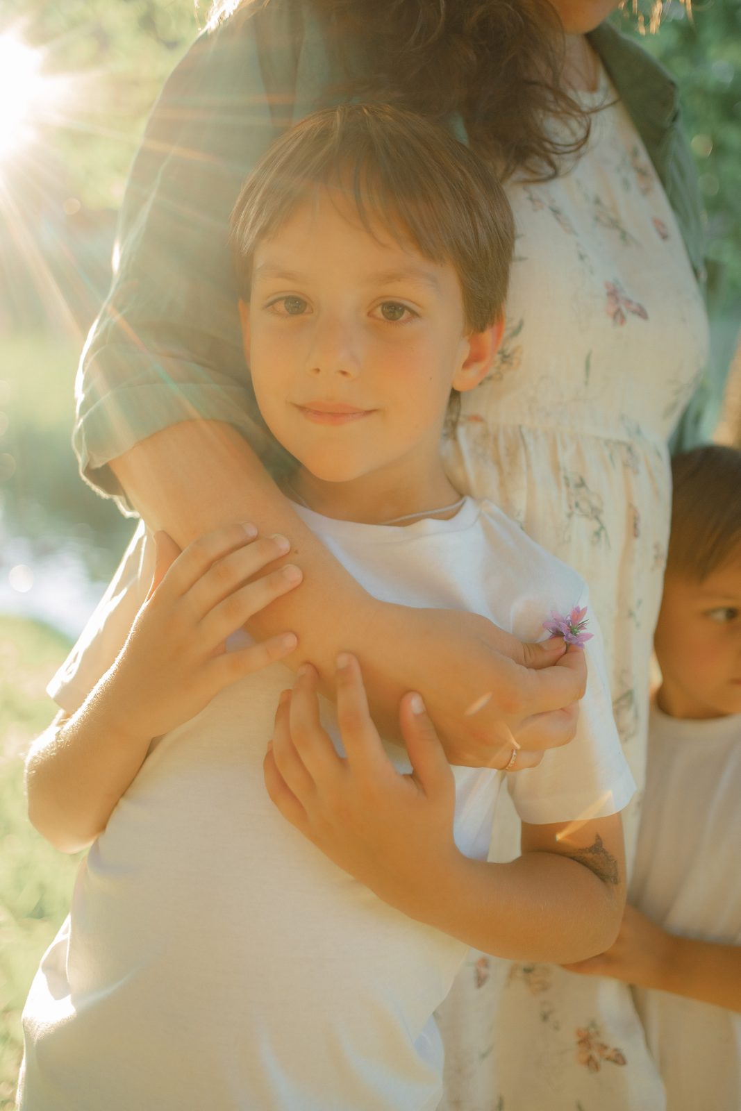 Boy hugging his mother's arm in backlit summer sun