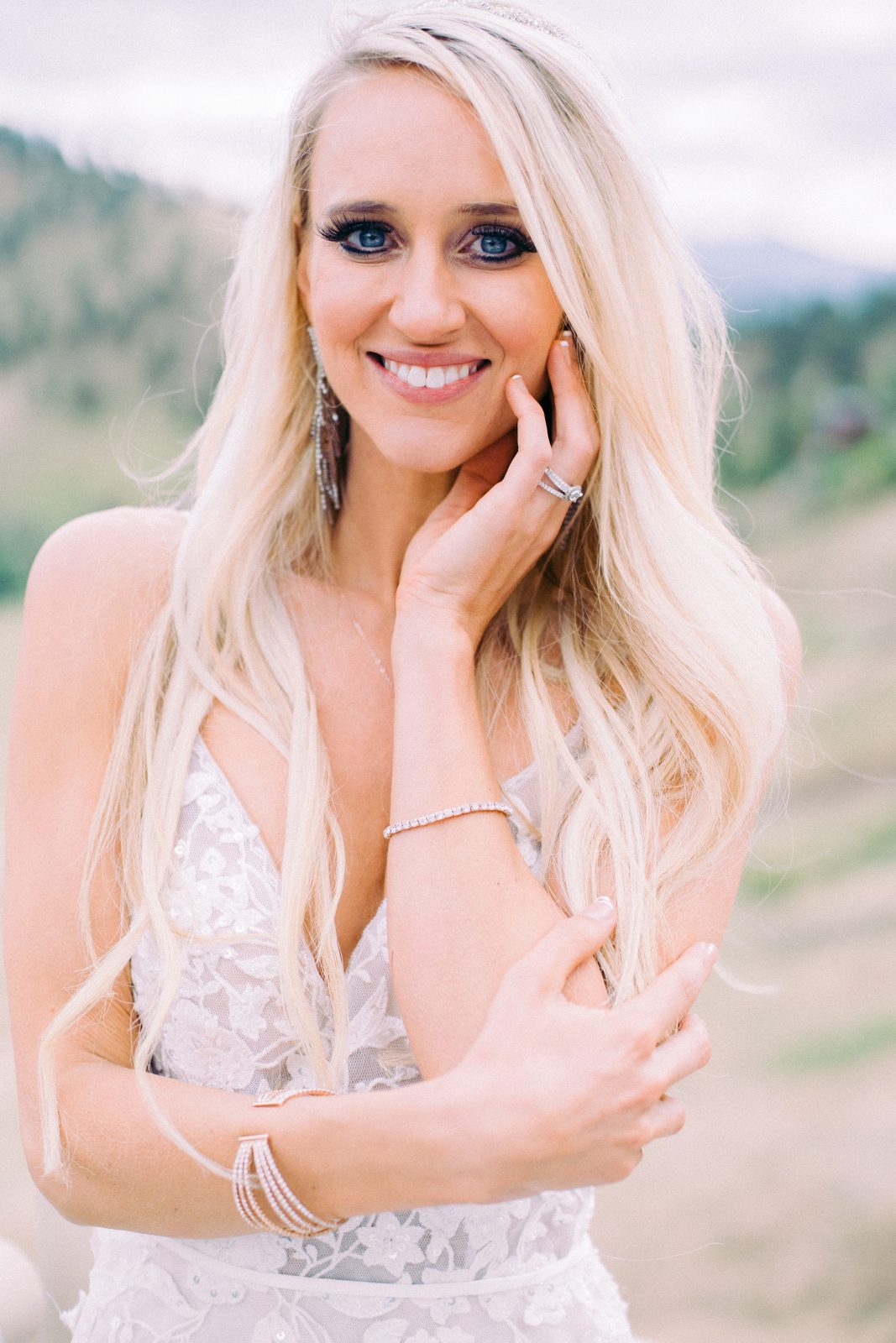 Smiling bride with crystal earrings and bracelets in the mountains