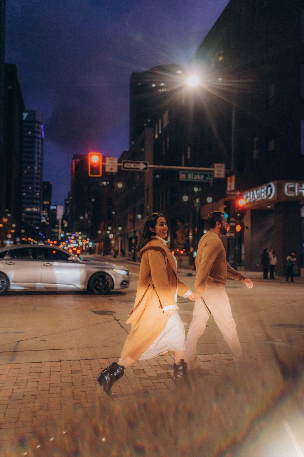Couple in camel coats crossing Blake Street at night