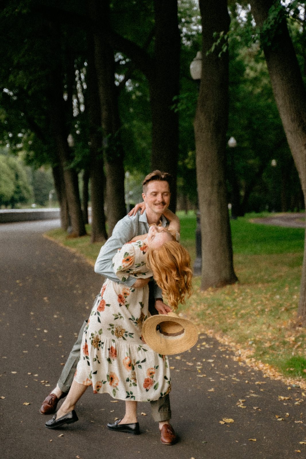 Man dipping his laughing partner on a tree-lined park path