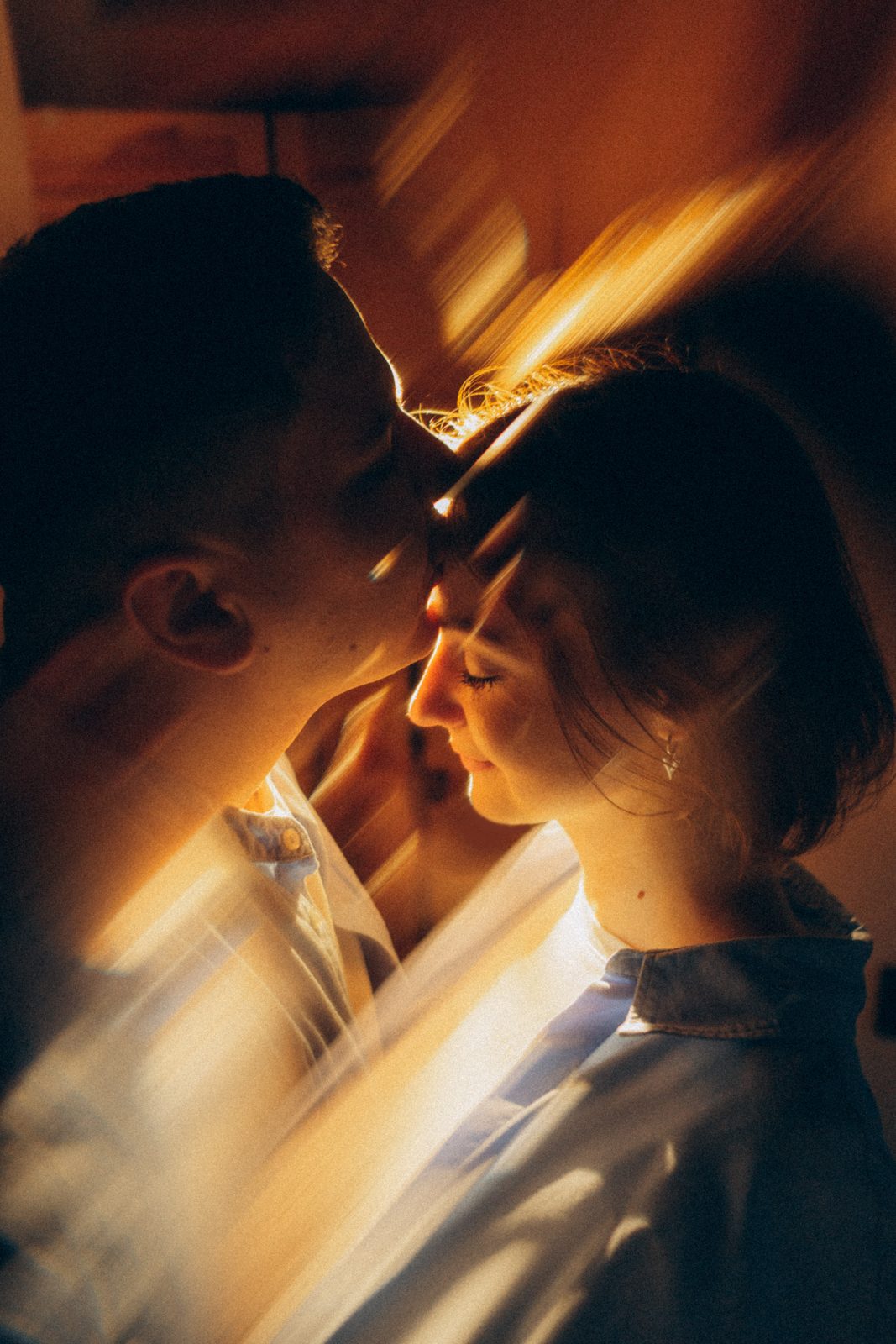 Couple touching foreheads in streaks of golden window light