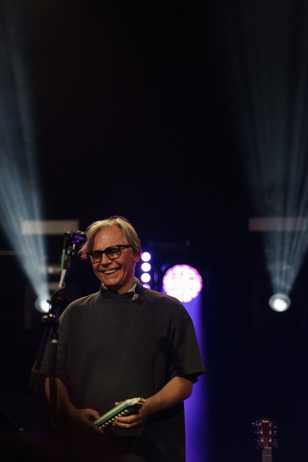 Musician laughing on stage, holding a melodica