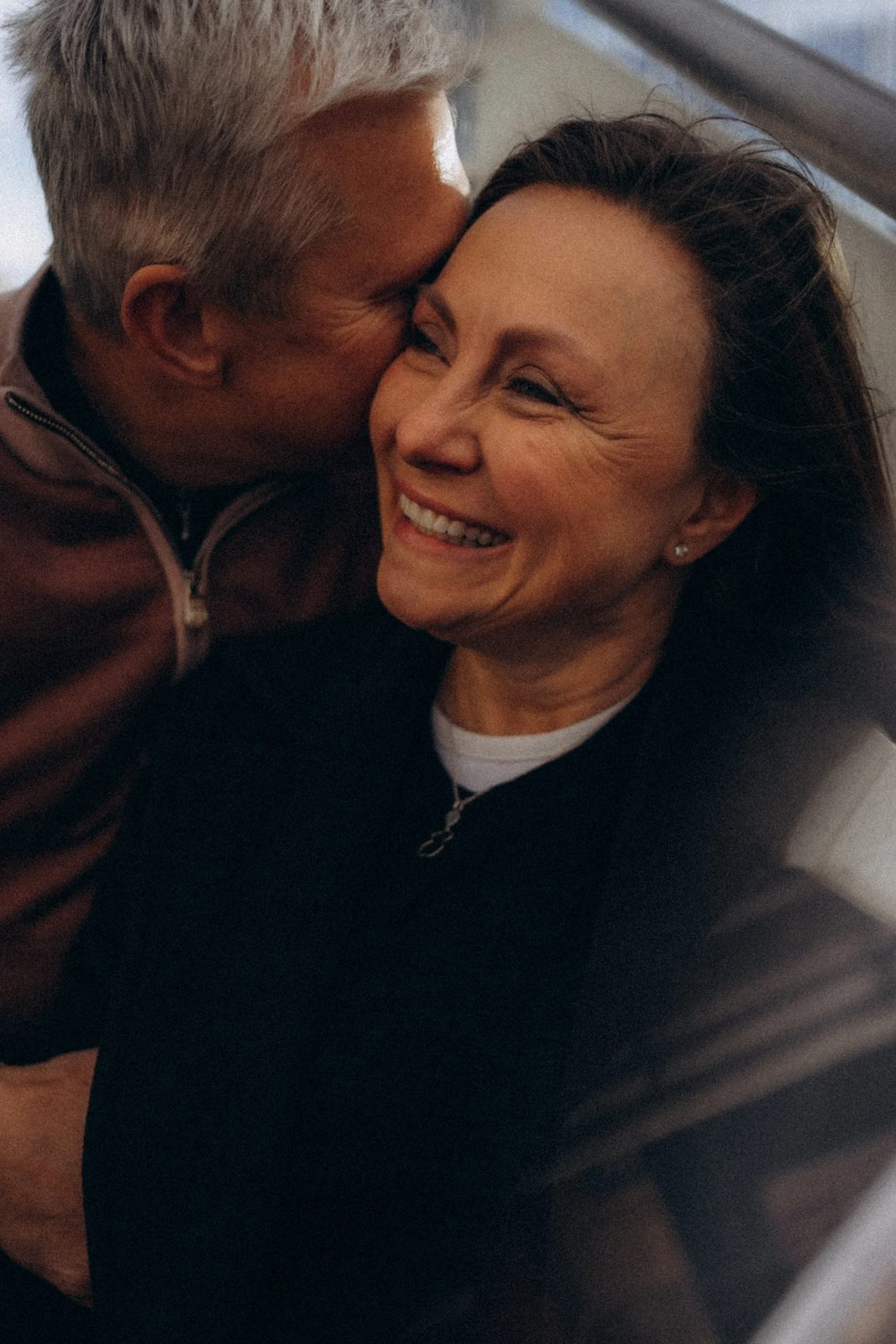 Silver-haired man kissing his laughing wife on the cheek