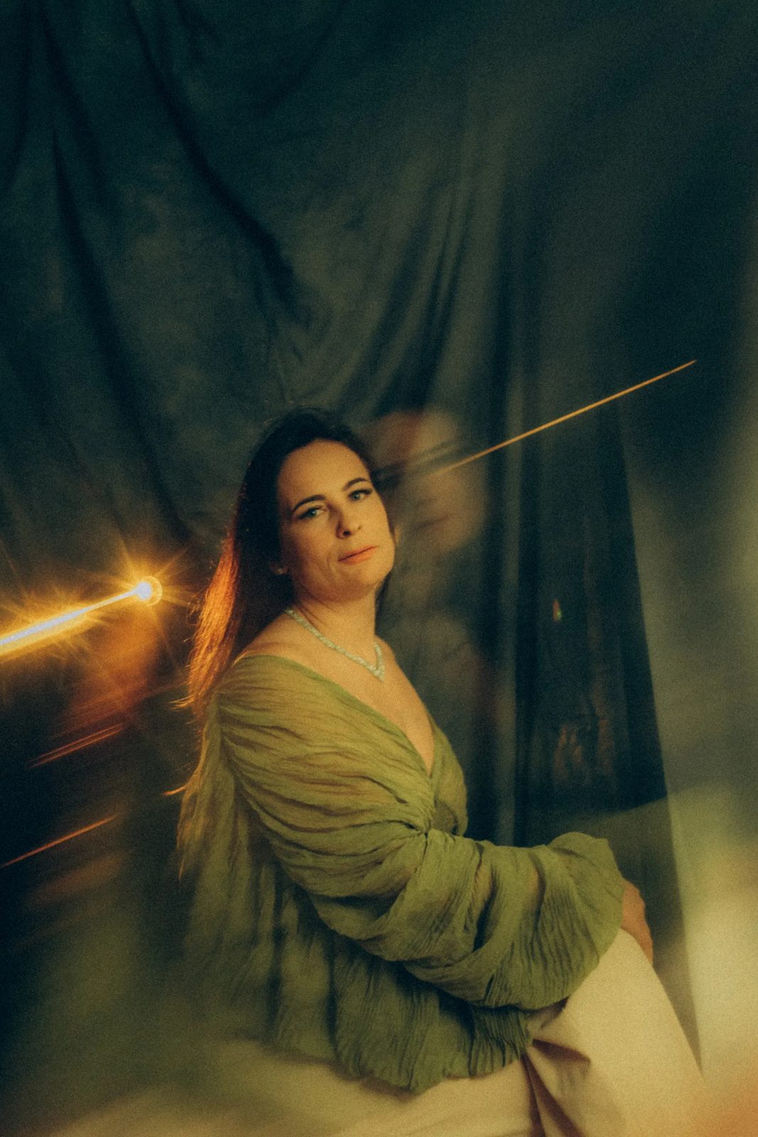 Woman in an olive dress with a streak of light across a green drape