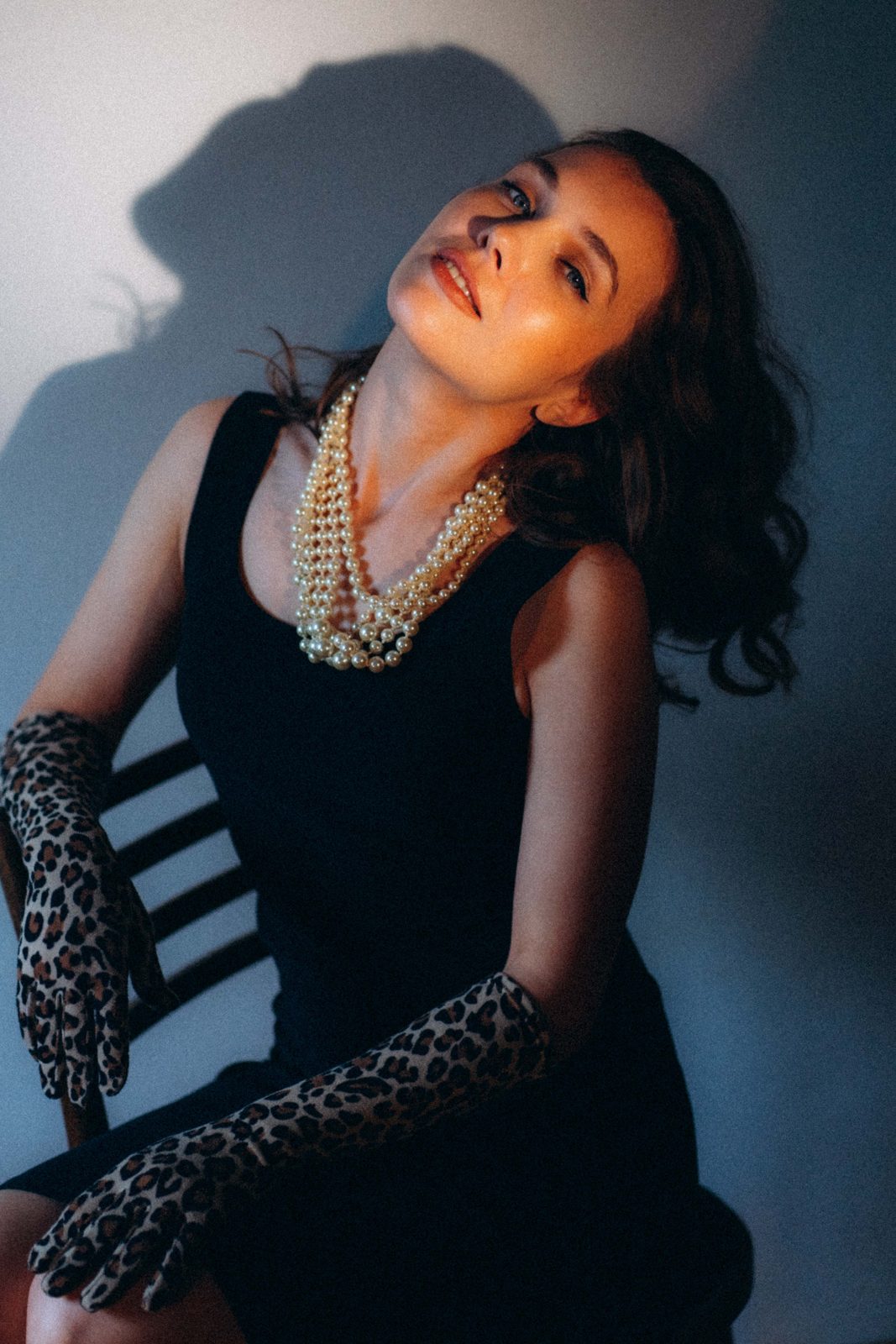 Woman in pearls and leopard gloves leaning back against a blue wall