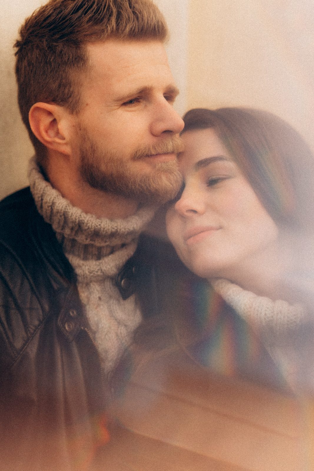 Couple resting cheek to cheek, softened by a prism flare
