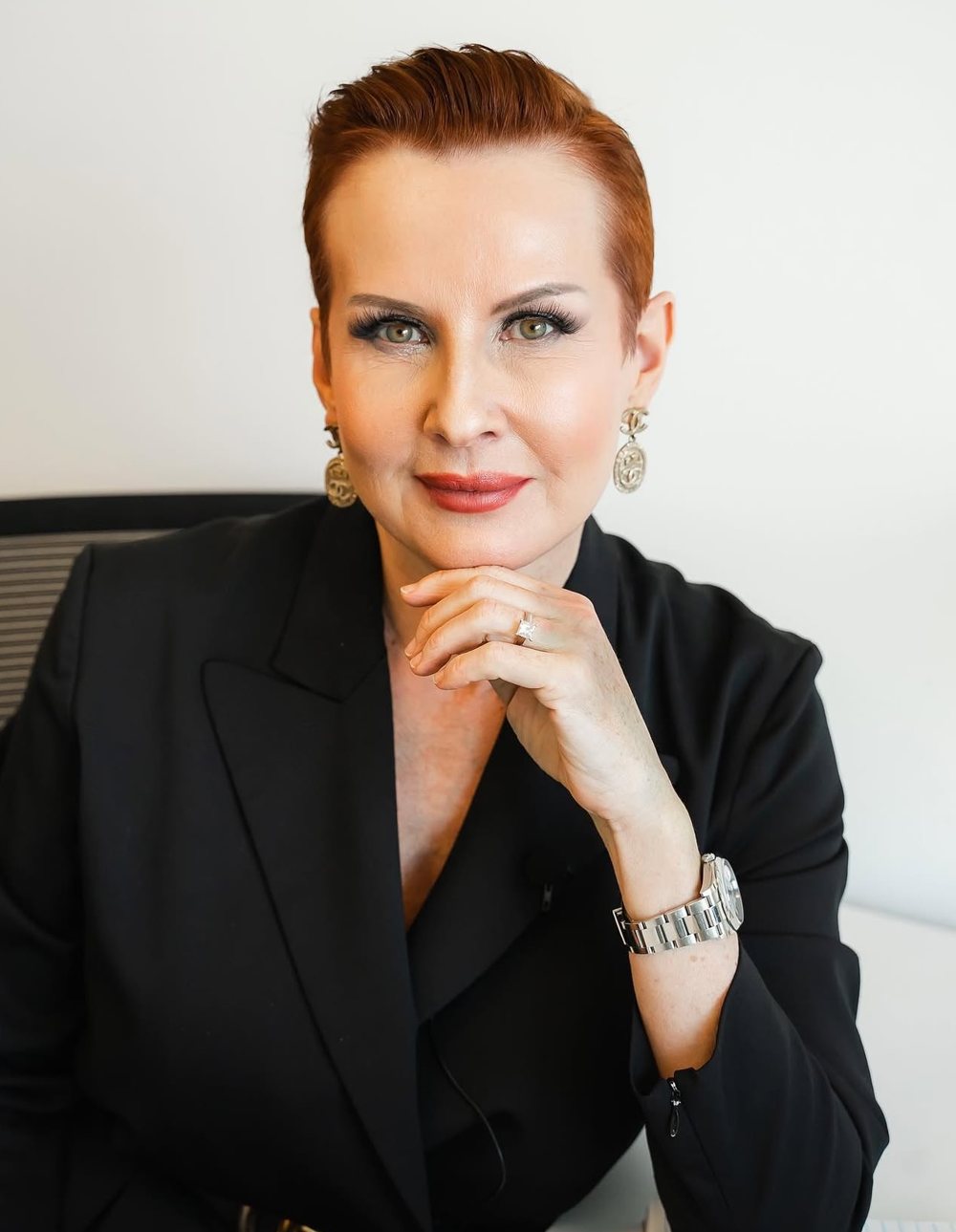 Real estate agent with short red hair in a black blazer, chin resting on her hand