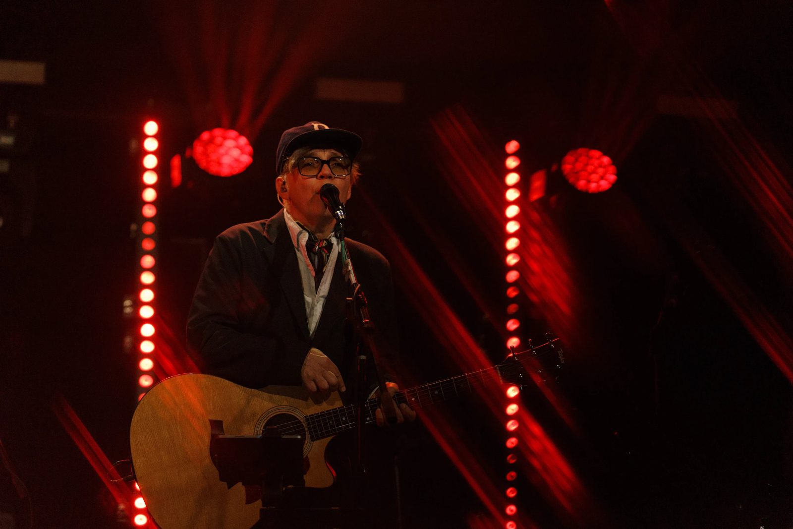 Singer with an acoustic guitar between red light bars