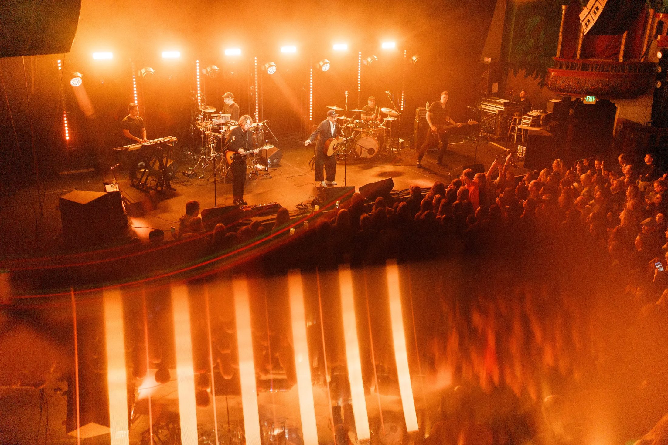 Band on an amber-lit stage seen from the balcony over the crowd