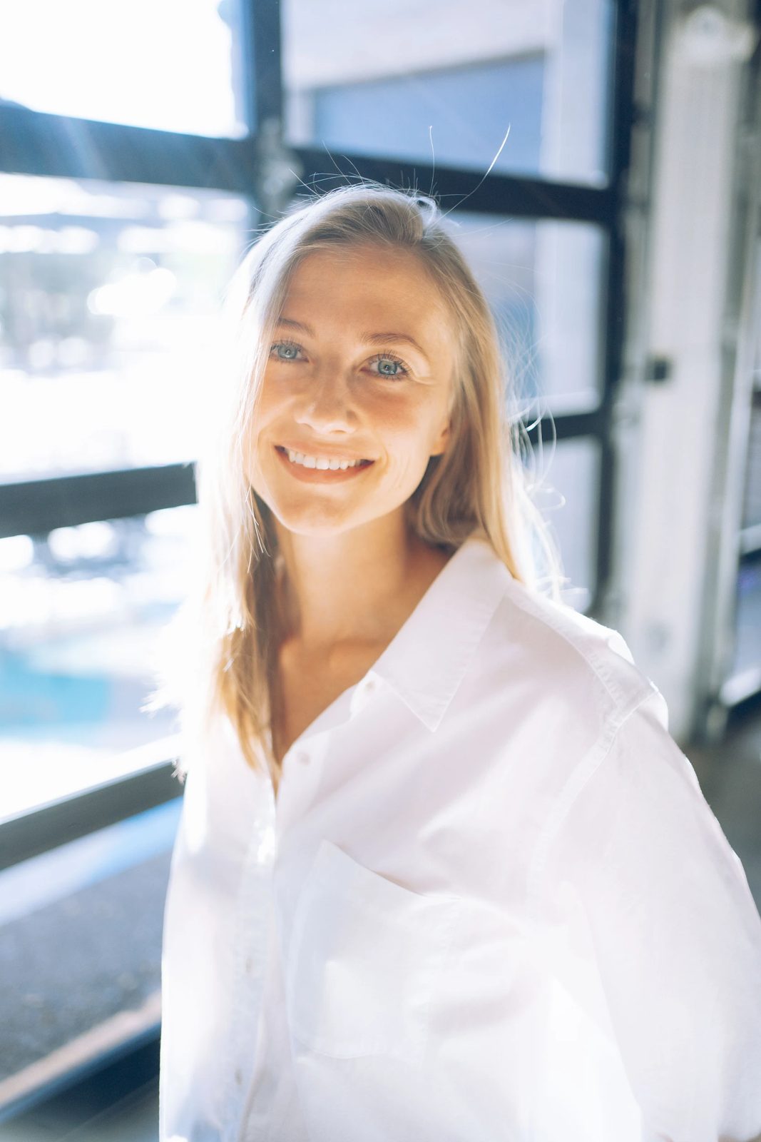 Smiling woman in a white shirt by a sunlit window