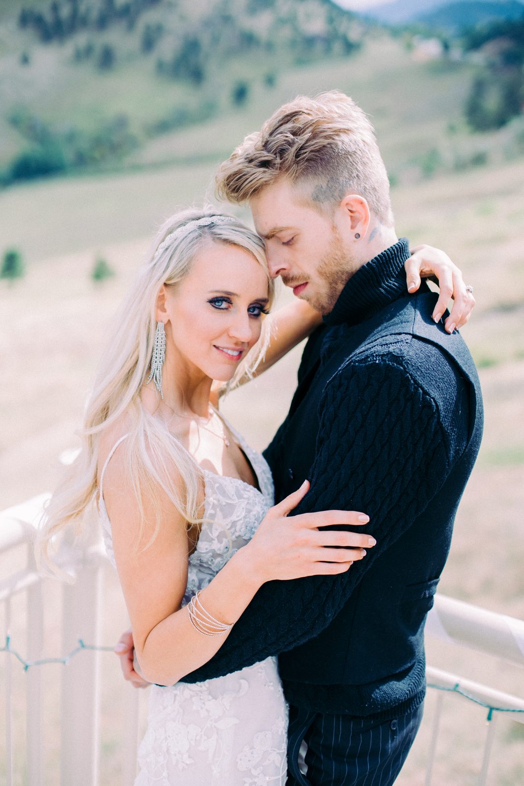 Bride with crystal earrings embracing her groom on a mountain terrace
