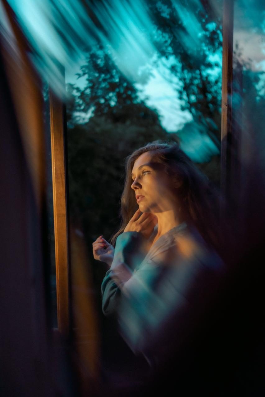 Woman by a window at dusk, framed by blue and amber light